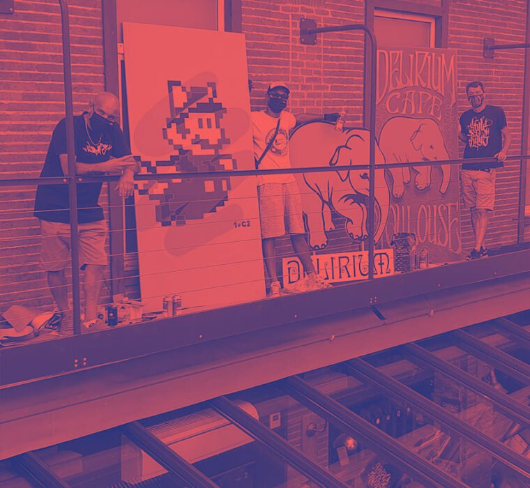 Artistes peignant une fresque au Delirium Café, avec des éléphants et un personnage de jeu vidéo.