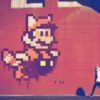 Mur peint style pixel-art sur fond rouge, représentant un personnage de jeu vidéo. Couleurs vives et graphisme urbain. Murals-4.jpg
